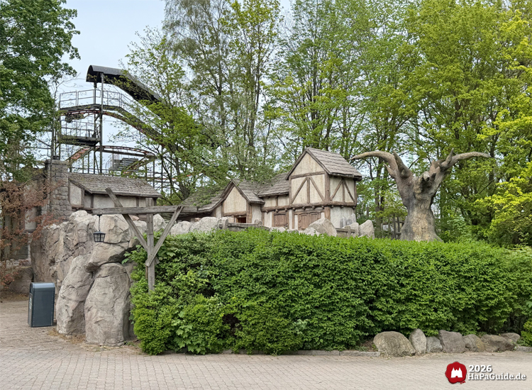 Thematisch gestaltete Häuserfassaden Roanoke Siedlung im Bereich Abenteuerland im Hansa-Park mit Felsen, Baumskulptur und grüner Bepflanzung