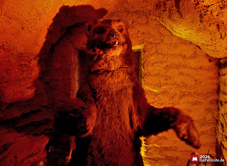 Große Bärenfigur in der Bärenhöhle des Hansa-Parks, steht aufrecht in einer Felskammer mit warmem orangefarbenem Licht, wirkt lebensecht und eindrucksvoll