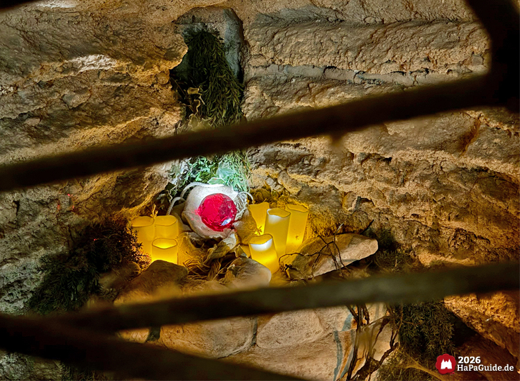 Leuchtender roter Kristall in der Bärenhöhle des Hansa-Parks, umgeben von künstlichen Kerzen und Moos, eingebettet in eine steinerne Nische