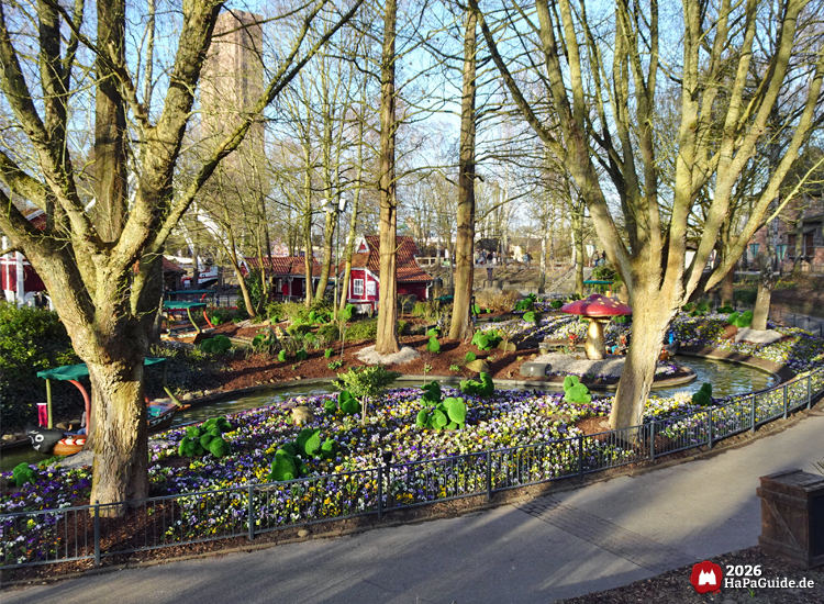Blumenreich gestalteter Gartenbereich im Hansa‑Park mit bunten Beeten, Wasserlauf, Felsen und dekorativen Figuren auf dem Alten Jahrmarkt