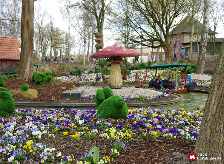 Blumenmeerbootsfahrt im Hansa‑Park durch farbenfrohe Blumenlandschaft mit Rasen-Hasen, großem Fliegenpilz und familienfreundlicher Gartenszenerie
