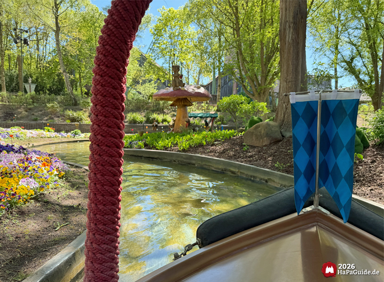 Bootsfahrt im Blumenmeer des Hansa-Parks mit Blick auf einen großen Pilz und bunte Blumenbeete, umgeben von grünen Bäumen und sonnigem Wasserkanal