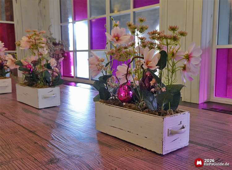 Dekorative Blumenarrangements in weißen Holzkästen mit pink-violetten Fenstern im Café Rosa im Hansa-Park