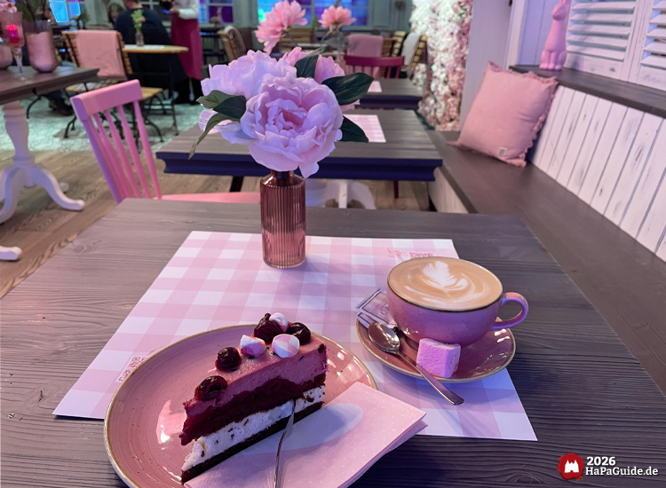 Tortenstück und Latte Art auf rosa Geschirr in gemütlichem Café Rosa im Hansa-Park mit floraler Dekoration