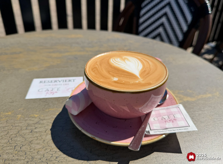 Cappuccino mit Herz-Latte-Art in rosa Tasse auf reserviertem Tisch der Außenterrasse des Café Rosa im Hansa-Park