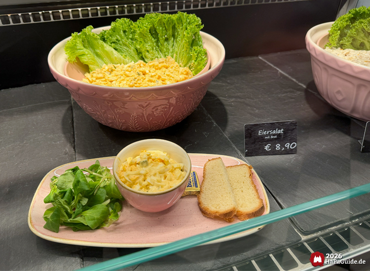 Vitrine im Café Rosa des Hansa-Parks mit Eiersalat in rosa Schüssel, serviert mit Brot, Butter und frischem grünen Salat, daneben Preisschild mit €8,90