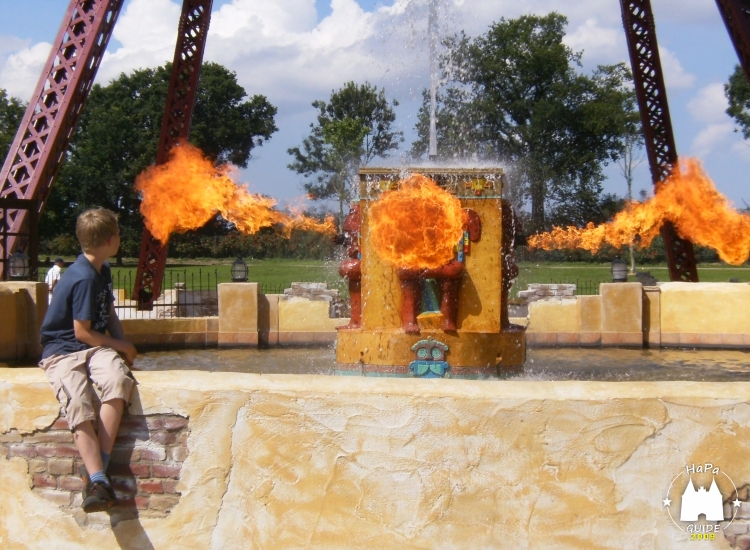Ein Junge sitzt auf einer Mauer während aus einem Brunnen Flammen hervorstoßen