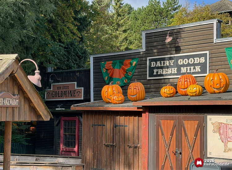 Holzgebäude im Westernbereich des Hansa-Parks mit Kürbisdekoration auf dem Dach, Schilder Dairy Goods Fresh Milk und New Lübeck Goldmine, grüne und orange Girlanden unter Herbstsonne