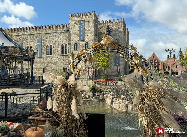 Steinerner Palacio de Braga im Hansa-Park mit Erntedank-Dekoration aus Maiskolben und Pampasgras am Teich der Hanse in Europa, im Hintergrund Hanse-Karussell unter blauem Himmel