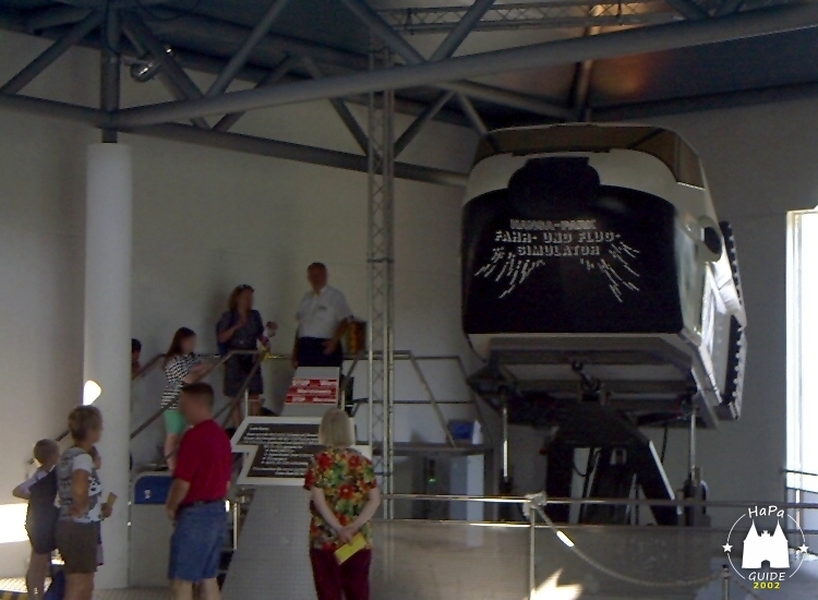 Besucher warten neben dem gerade fahrendem Fahr- und Flugsimulator
