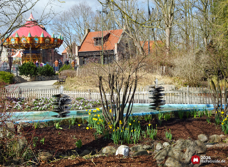 Frühlingshafte Parkszene mit Wasser-Schiffschrauben, Narzissen und Hanse-Flieger im Hintergrund