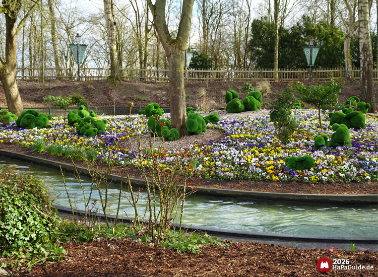 Blumenbeet mit bunten Stiefmütterchen und Rasen-Hasen am Kanal der Blumenmeerbootsfahrt im Hansa-Park