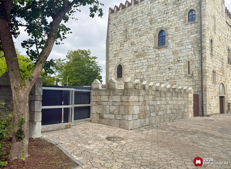 Seitliche Ansicht des Tors hinter dem Palacio de Braga im Hansa-Park mit hohen Mauern und Baum im Vordergrund, daneben die Burg mit kleinen Fenstern und Zinnen