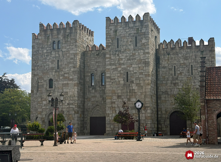 Große Burganlage Palacio de Braga im Hansa-Park mit hohen Türmen, Zinnen und steinernen Mauern, davor gepflasterter Platz mit Uhr, Bänken und Besuchenden bei sonnigem Wetter