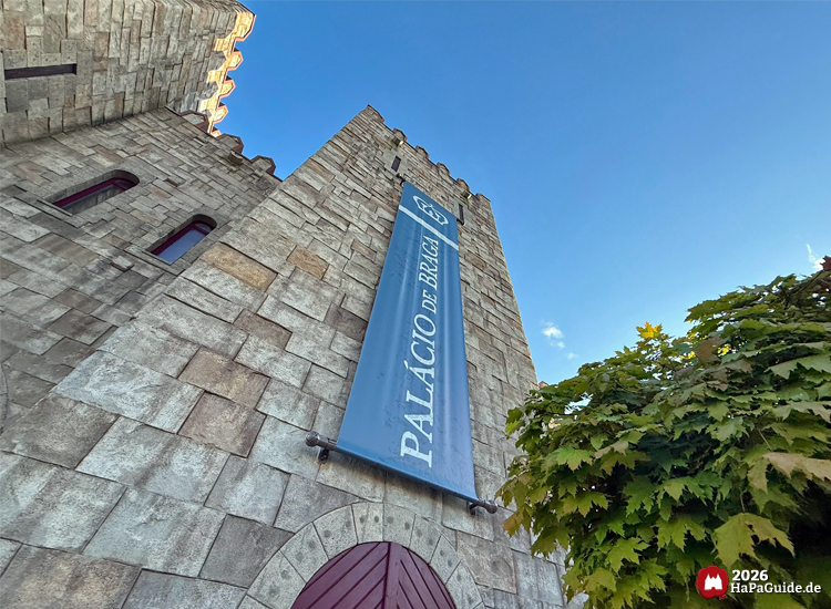 Nahaufnahme eines Turms des Palacio de Braga im Hansa-Park mit großem blauen Banner und Schriftzug Palácio de Braga, rote Tür und grüne Baumkrone im Vordergrund