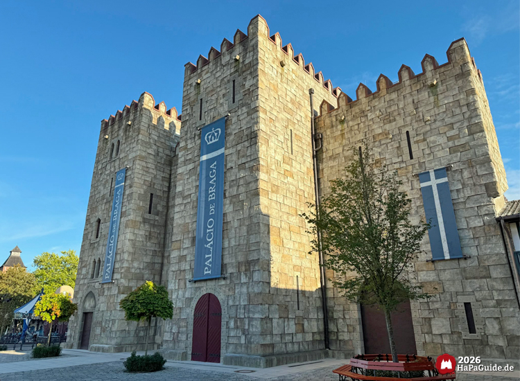 Seitliche Frontalansicht des Palacio de Braga im Hansa-Park mit hohen Türmen, Zinnen und blauen Bannern, gepflasterter Platz und Bäume im Vordergrund bei Abendsonne