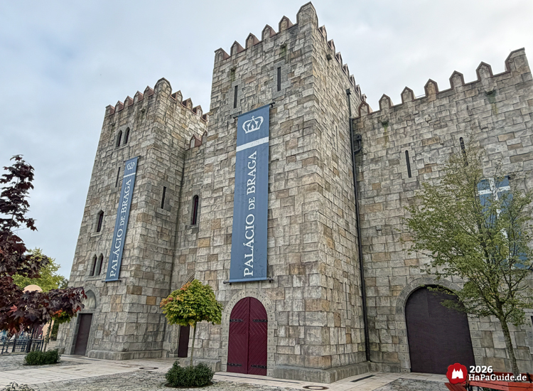 Palácio de Braga im Hansa-Park mit hohen Türmen, grauer Steinfassade und blauen Bannern mit weißer Schrift, mittelalterliche Architektur unter bewölktem Himmel