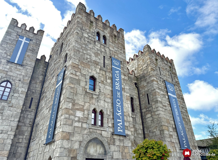 Palácio de Braga im Hansa-Park mit hohen Türmen, blauen Bannern und Zinnen, graue Steinfassade vor blauem Himmel mit weißen Wolken