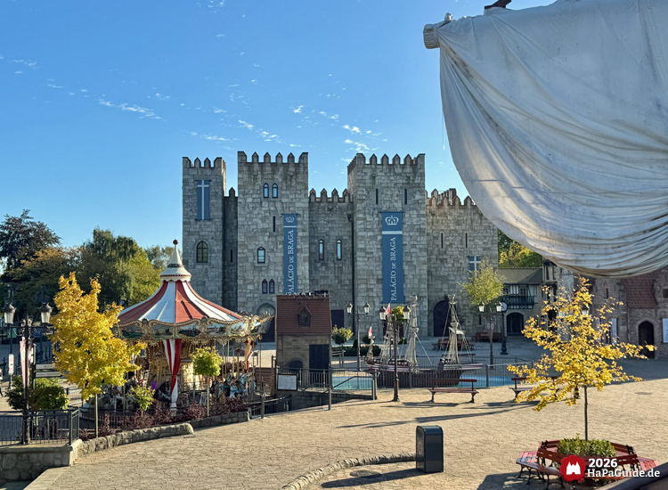 Palácio de Braga im Hansa-Park mit Hanse-Karussell und Segel der Hansekogge im Vordergrund, mittelalterliche Steinarchitektur und Herbstbäume unter klarem blauen Himmel