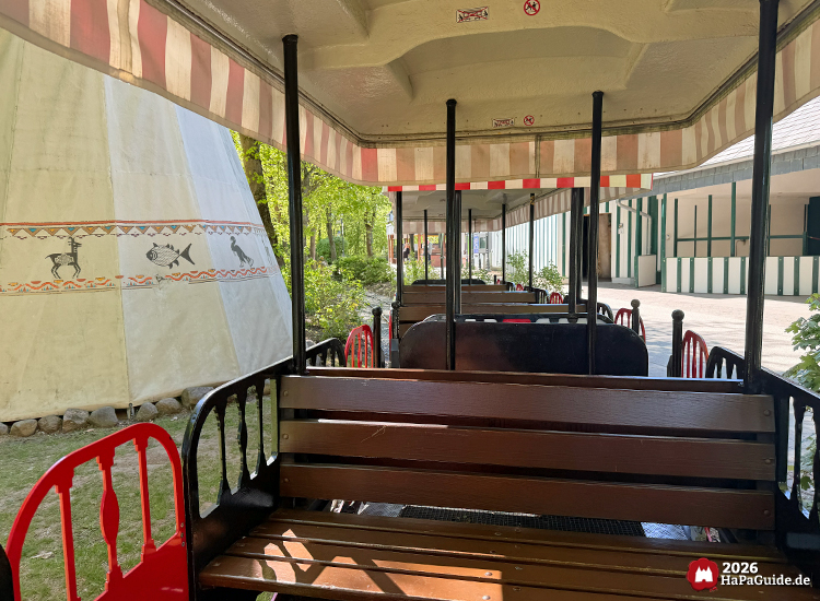 Innenansicht eines Waggons der Parkeisenbahn Hansa-Park Express im Hansa-Park mit Holzsitzbänken und rot-weiß gestreiftem Dach, neben einem Tipi mit indigenen Mustern und Tiermotiven