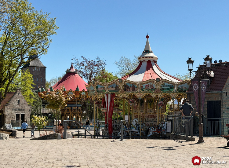 Historisches Hanse-Karussell im Hansa-Park mit rotem und weißem Dach, verzierten Malereien und goldenen Ornamenten, umgeben von Kopfsteinpflaster und Gebäuden im hanseatischen Stil
