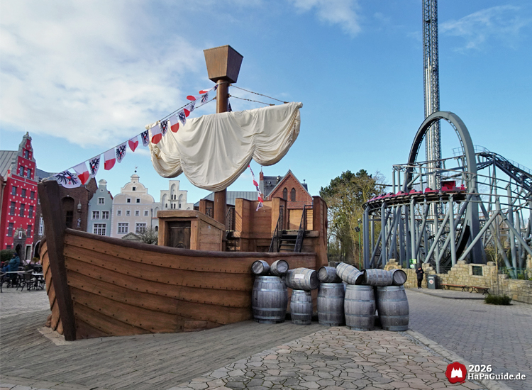 Hölzerne Hansekogge vor farbigen Giebelhäusern mit Nessies Looping und dem Royal Scotsman im Hansa Park