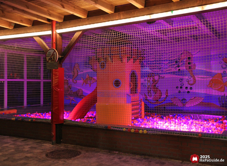 Beleuchteter Indoor-Spielbereich Hüpf- und Ballhaus im Hansa-Park mit Ballbecken, roter Rutsche und gelbem Turm vor einer Unterwasserwand mit Fischen und Seepferdchen