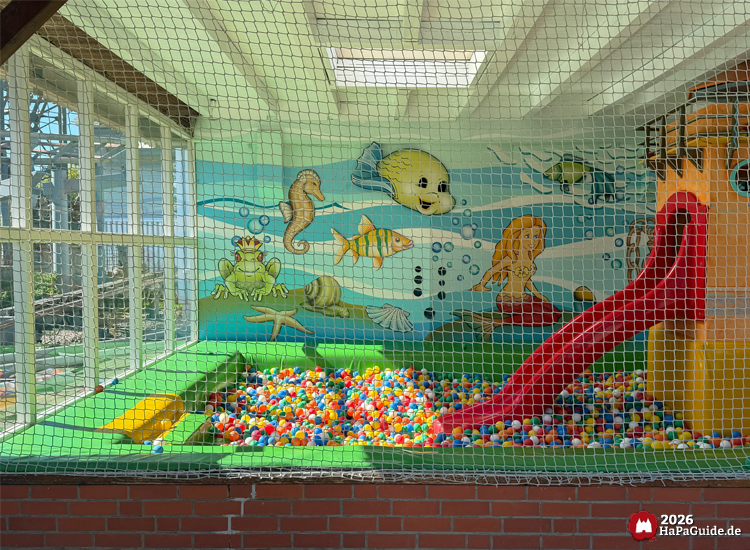 Indoor-Spielbereich im Bezaubernden Britannien des Hansa-Park mit buntem Ballbecken, roter Rutsche und Unterwasserwand mit Meerjungfrau, Fischen und Seepferdchen bei Tageslicht