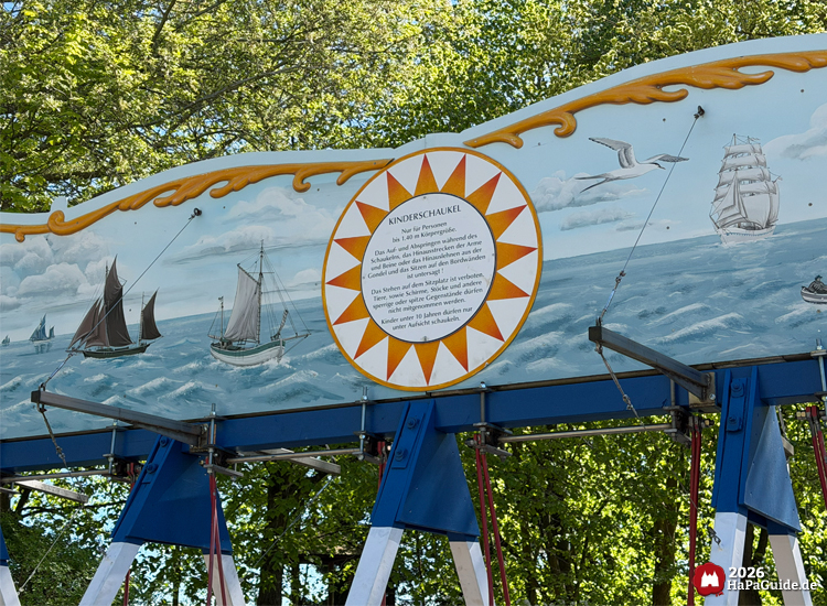 Bemalte Tafel der Kinder-Schiffschaukel im Hansa-Park mit Segelschiffen auf dem Meer, goldener Verzierung und rundem Textfeld mit Sicherheitshinweisen für Kinder