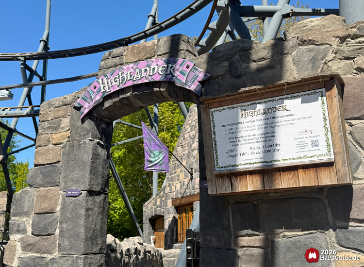 Eingang zur Attraktion Highlander im Hansa-Park mit steinernem Torbogen, lila kariertem Schild und Informationstafel zu den Fahrprogrammen Tilt und Super-Tilt