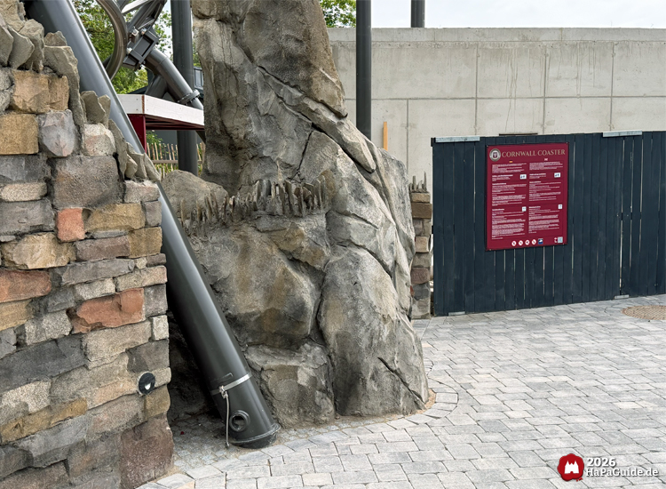 Felsenlandschaft und Baustellenbereich des Cornwall Coaster im Hansa-Park mit grauen künstlichen Felsen, Rohrleitung und rotem Hinweisschild mit Sicherheitsinformationen