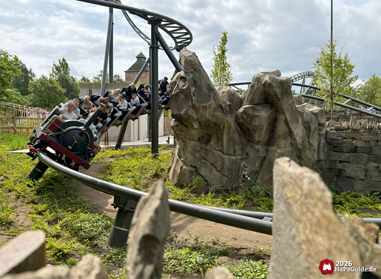 Zug des Cornwall Coaster im Hansa-Park fährt durch eine Kurve zwischen künstlichen Felsen, thematisiert als kleine Dampflok mit Fahrgästen, umgeben von Grün und Holzzaun am zukünftigen Roche Rock