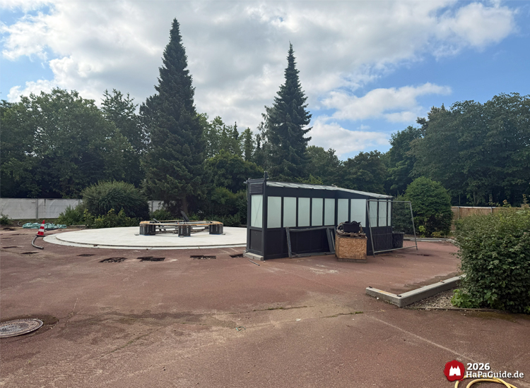 Runde Betonplattform mit ehemaliger Glaskonstruktion des Holsteinturms im Bauabschnitt der Hansa-Park Neuheit 2027, umgeben von Bäumen und rotem Bodenbelag unter leicht bewölktem Himmel