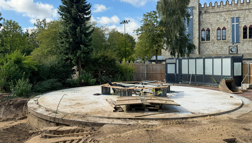 Zu den Neuheiten 2027 Baustelle des Buddenbrook-Turms im Hansa-Park mit rundem Betonfundament und Baumaterialien, im Hintergrund der Palácio de Braga mit roten Fenstern und blauen Bannern