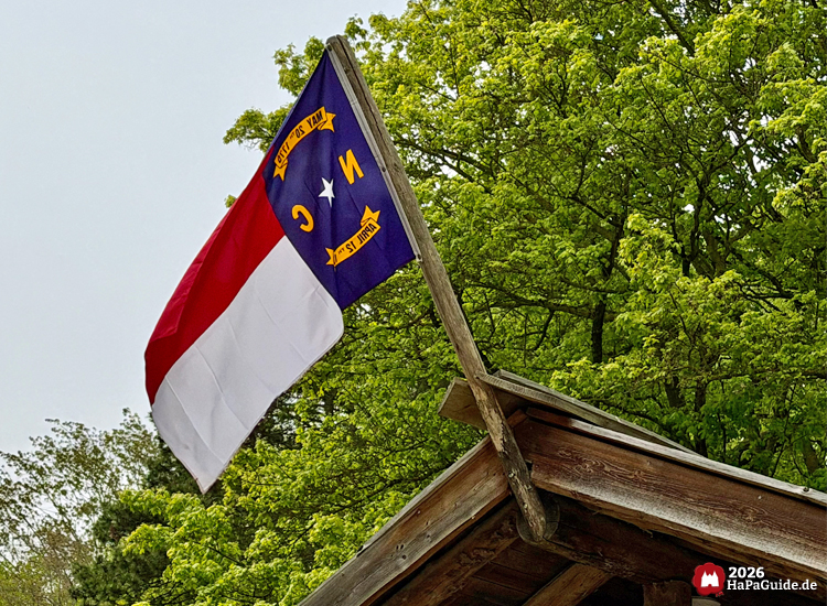 Flagge des US-Bundesstaates North Carolina auf dem Dach des Kiosks Tipi-Lager im Hansa-Park, umgeben von grünen Bäumen