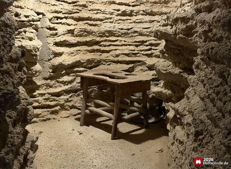 Rustikaler Tisch mit Aussparungen in der steinernen Bärenhöhle im Hansa-Park, beleuchtet durch warmes Licht