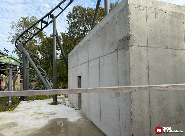 Großer Betonbau des Cornwall Coaster im Hansa-Park mit grauen Wänden und sichtbaren Fugen, daneben geschwungene Achterbahnschiene und grüne Bäume unter leicht bewölktem Himmel