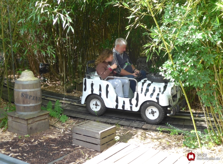 Ein Jeep fährt an Kisten und Fässern vorüber durch Bambus