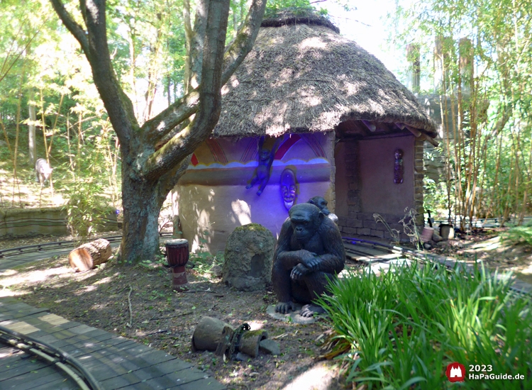 Ein Gorilla sitzt vor einer runden, afrikanischen Lehmhütte