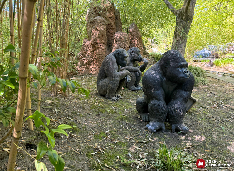 Drei Gorillafiguren im Themenbereich Alter Jahrmarkt der Safari-Jeeps im Hansa-Park, umgeben von Bambus und Termitenhügeln, natürliche Dschungelkulisse mit grünem Licht