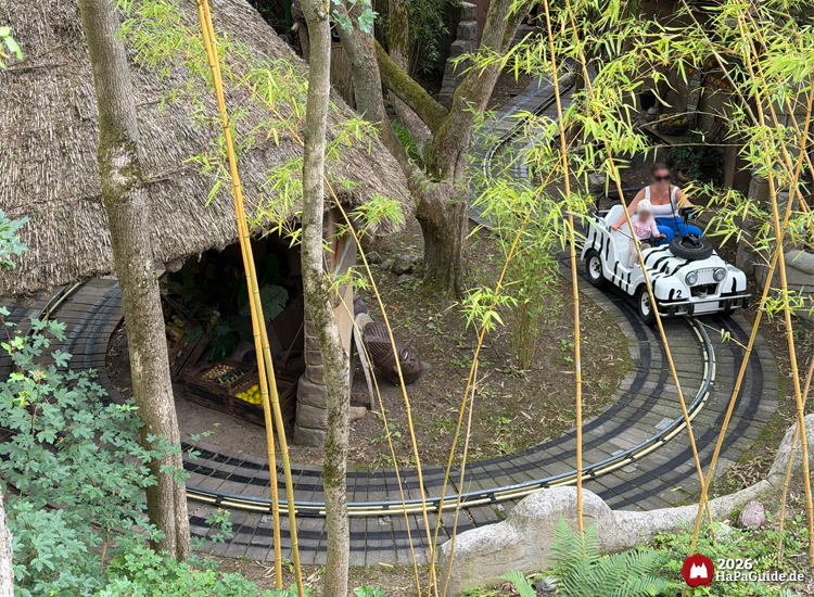 Zebra gestreifter Safari-Jeep im Hansa-Park fährt an einer afrikanischen Strohhütte vorbei, umgeben von Bambus und Bäumen, im Inneren Dekoration mit Früchten und Figuren