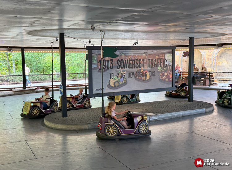 Kinder fahren Oldtimer-Autoscooter auf der 1903 Somerset Traffic Bahn im Hansa-Park, im Hintergrund Banner mit der Aufschrift '1903 Somerset Traffic Teil 2 der Thematisierung folgt'