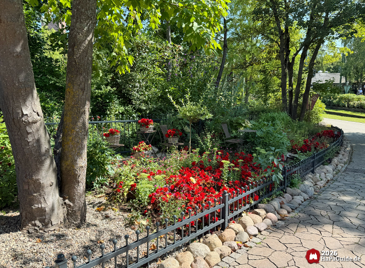 Blühender Garten im Hansa-Park Hansa-Garten mit roten Blumen entlang eines gepflasterten Weges, umgeben von Bäumen und Sträuchern, ruhige Atmosphäre im Sommerlicht