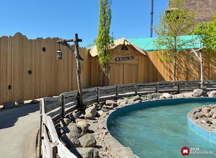 Wasserkanal der Attraktion Störtebeker’s Kaperfahrt im Hansa-Park mit blauer Rinne und Holzgeländer, daneben ein Gebäude mit der Aufschrift 'Störtebeker' und hölzerner Palisadenwand