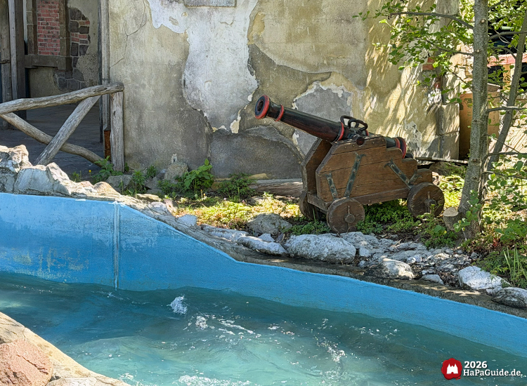 Holzkanone mit schwarzen Metallbeschlägen neben der Wasserbahn Störtebeker’s Kaperfahrt im Hansa-Park, steht vor einer verwitterten Wand mit sichtbaren Backsteinresten