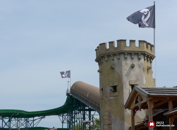 An Burgturm und Rampe wehen Totenkopfflaggen mit Trinkkrug und Säbel