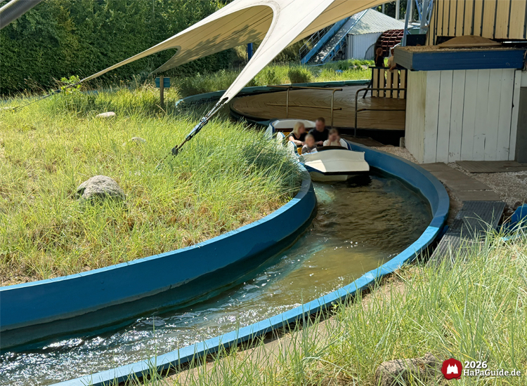 Boot der Wildwasserbahn Super Splash im Hansa-Park fährt durch Kanal aus weißem Zeltdach, umgeben von Dünengras, sonniger Tag mit klarer Beleuchtung