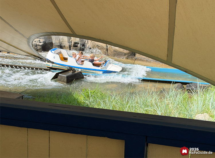 Boot der Attraktion Super Splash im Hansa-Park beim Eintauchen ins Wasser nach der Abfahrt, spritzendes Wasser unter weißem Zeltdach, Fahrgäste genießen die Abkühlung