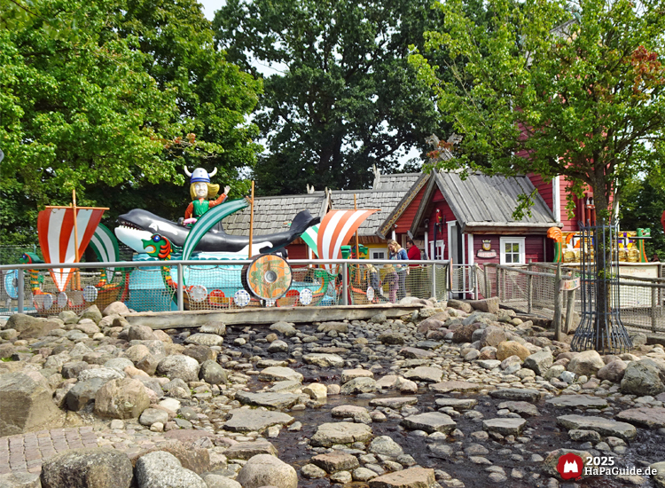 Wikinger-Bootsfahrt - Fahrgeschäft hinter einem Wasserlauf