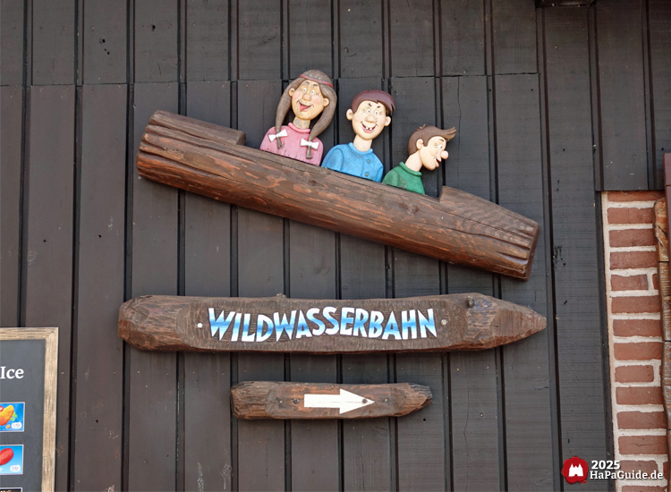 Holzschild zur Wildwasserbahn im Hansa-Park mit geschnitztem Baumstamm-Motiv und Wegweiser-Pfeil